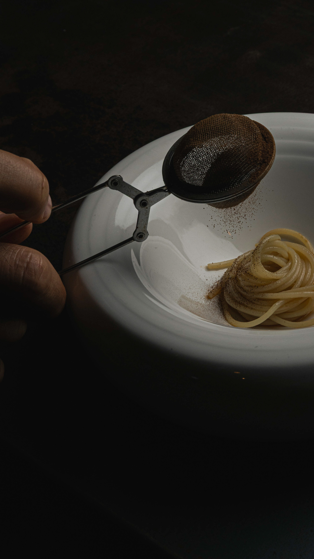 Chef rifinisce un piatto di spaghetti con una polvere setacciata al passe